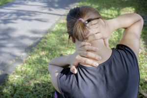 Female runner rubbing sore muscles in her neck and upper back after a workout