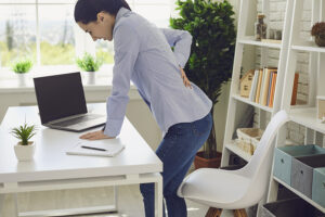 Woman experiencing low back pain while standing at her desk at work
