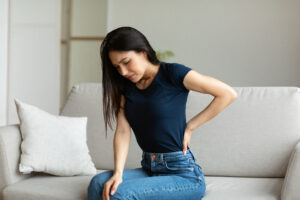 Woman sitting on couch at home touching her painful lower back