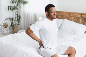 Man sitting on the edge of his bed and touching his aching back