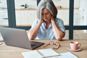 Tired woman sitting in front of laptop massaging her painful neck