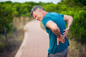 Athletic man on running path leaning over with back pain