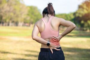 Young female runner pausing on path and touching her painful low back