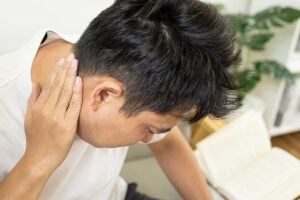 Man leaning over a book and rubbing his painful neck