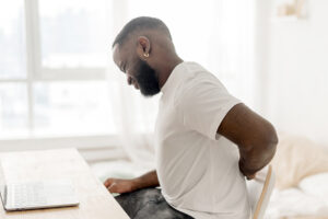 Man experiencing low back pain while seated at desk in front of a computer