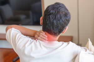 Man experiencing neck pain while sitting on sofa at home