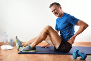 Athletic man experiencing low back pain while working out on floor mat in gym